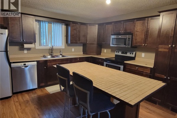 Kitchen view showing stainless steel appliances, dark wood cabinets, and island seating. - 4705 Tribune Street, Macklin