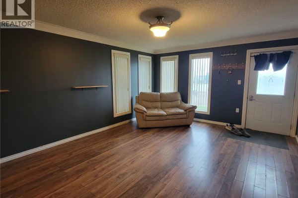 Living room with dark gray walls, laminate flooring, and a beige loveseat. - 4705 Tribune Street, Macklin