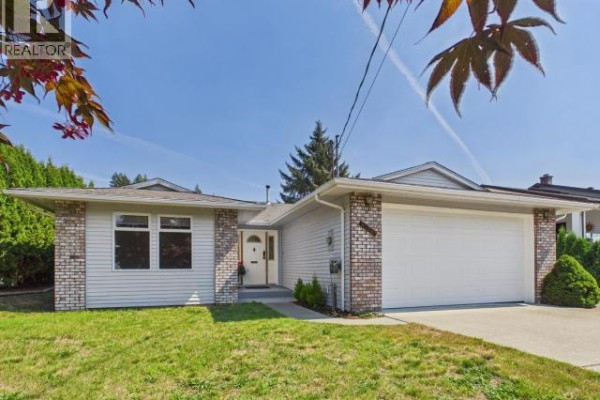 Exterior front view of a light blue house with a white garage door and green lawn. - 4706 Ontario Ave, Powell River