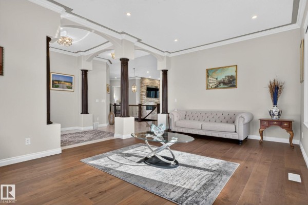 Living room with dark hardwood floors, a gray sofa, glass coffee table, and a patterned area rug. - 4707 Woolsey Cm Sw, Edmonton