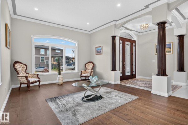 Living room with dark hardwood floors, two antique chairs, a glass coffee table, and a large arched window. - 4707 Woolsey Cm Sw, Edmonton