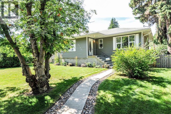 Concrete pathway leading to the front entrance of the house with manicured lawn and mature trees. - 4708 47 Street, Camrose