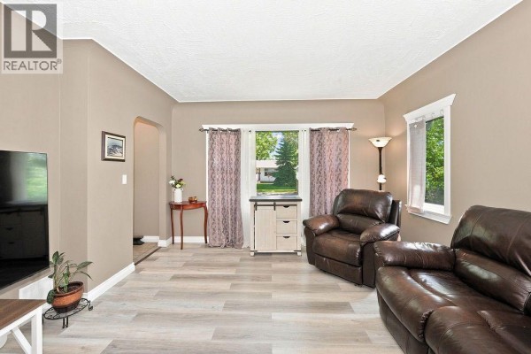 Living room with two recliners, a sofa, and a window with patterned curtains. - 4708 47 Street, Camrose