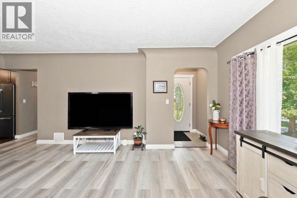 Living room showing a large television, an entryway, and a dining area with counter seating. - 4708 47 Street, Camrose