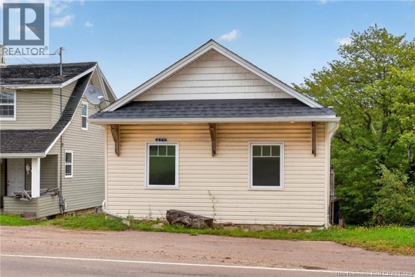 A beige residential building with a peaked roof and white trim, showing two windows and decorative wooden brackets. - 471 & 475 Centrale, Memramcook