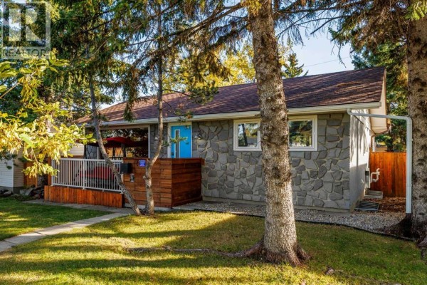 Side view of a bungalow with stone exterior, red swing on the deck, and wooden fence. - 4711 26 Avenue Sw, Calgary
