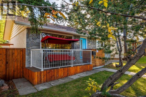 Wooden deck with a red swing and white railing overlooks the front lawn of the house. - 4711 26 Avenue Sw, Calgary