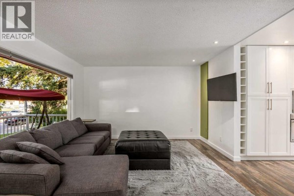 Living room with a large grey sectional sofa, ottoman, and built-in white cabinets. - 4711 26 Avenue Sw, Calgary