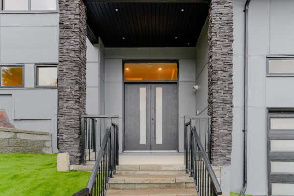 Double front doors with vertical silver accents, flanked by stone pillars and metal railings. - 47136 Sylvan Drive, Promontory, Chilliwack