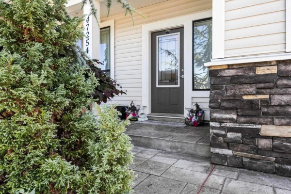 Covered front porch with a dark grey door, large windows, and patterned concrete floor. - 47254 Sylvan Drive, Promontory, Chilliwack