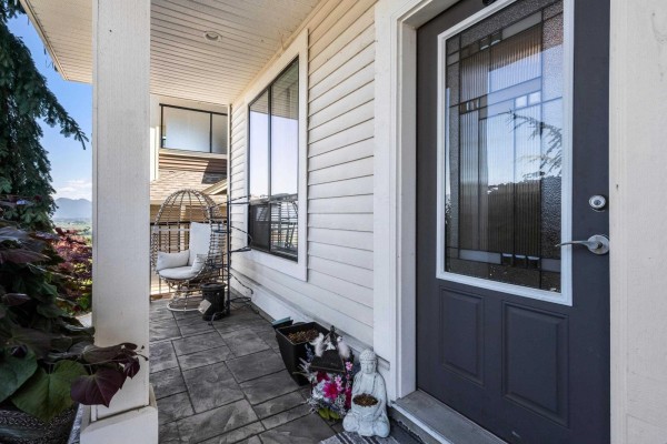 Living room with a stone fireplace, large windows, sliding glass doors, and comfortable seating. - 47254 Sylvan Drive, Promontory, Chilliwack