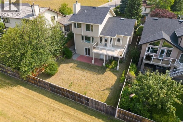 Aerial view of the backyard of a beige house, showing a deck, patio, and fence. - 473 Hawkford Way Nw, Calgary