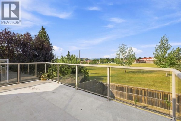 Concrete deck with glass railing overlooking a green park and trees. - 473 Hawkford Way Nw, Calgary