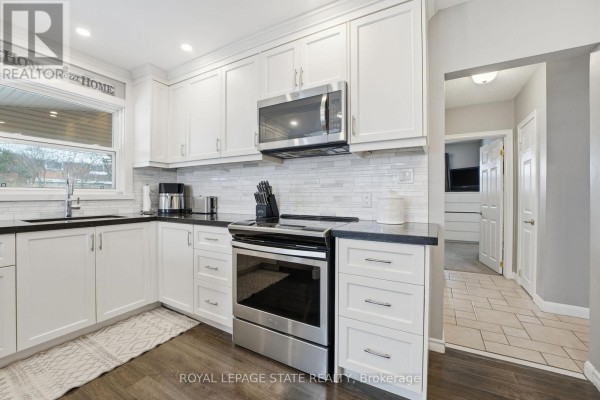 Modern kitchen with white cabinets, granite counters, breakfast bar, and stainless steel appliances - 473 Mohawk Road W Hamilton