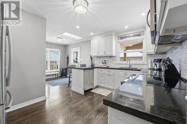 Stainless steel refrigerator and range in a modern kitchen with white cabinets and dark countertops - 473 Mohawk Road W Hamilton