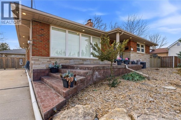 Aerial view of a brick bungalow with a detached garage and a large asphalt driveway. - 473 Mohawk Road W, Hamilton