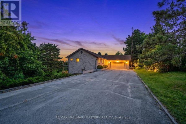 Grey brick house with a double car garage illuminated at dusk with a paved driveway surrounded by trees. - 473 Sunset Crescent, Alnwick/haldimand