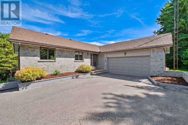 Front exterior of a grey brick house with a light tan garage door and landscaping in the front yard. - 473 Sunset Crescent, Alnwick/haldimand