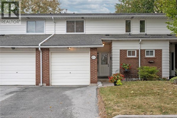 Close-up exterior front view of a townhouse unit with red brick and white siding, featuring a front door and garage. - 473 Woodview Road Unit# 2, Burlington