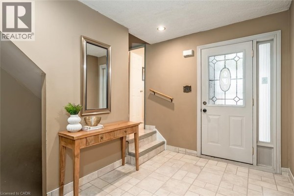 Interior entryway with beige walls, tiled floor, a wooden console table, a mirror, and a front door. - 473 Woodview Road Unit# 2, Burlington