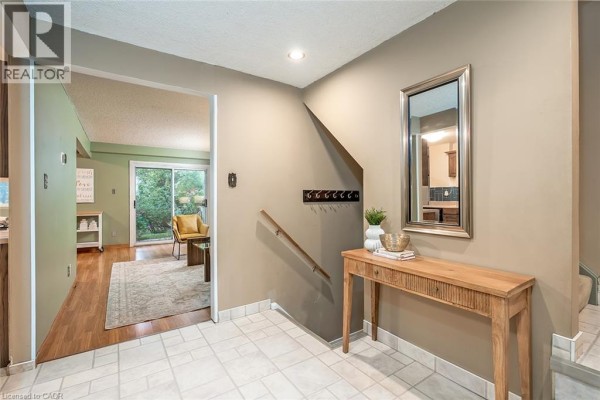 Interior entryway with beige walls, tiled floor, a wooden console table, a mirror, and a view into a living room. - 473 Woodview Road Unit# 2, Burlington
