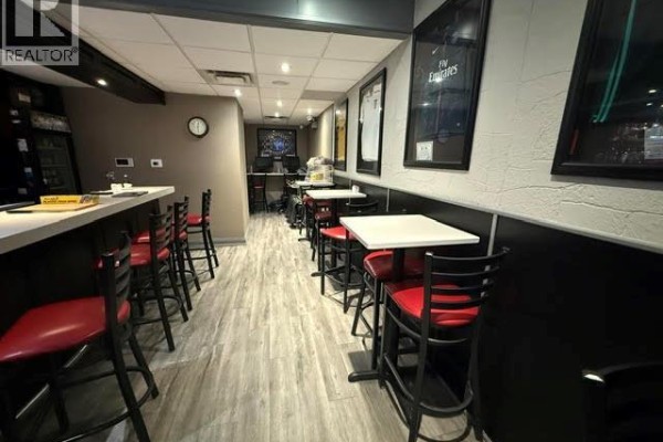 Long view of the bar and dining area showing multiple tables, chairs, and framed jerseys. - 4736 Valley Way, Niagara Falls