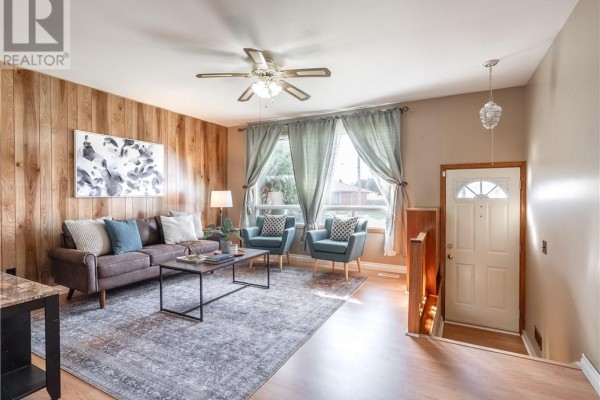 Living room with brown sofa, two blue chairs, patterned rug, and wood-paneled wall. - 4738 Fergus Avenue, Greater Sudbury