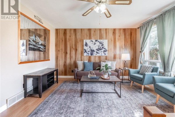 Living room with brown sofa, two blue chairs, large mirrored wall art, and wood paneling. - 4738 Fergus Avenue, Greater Sudbury