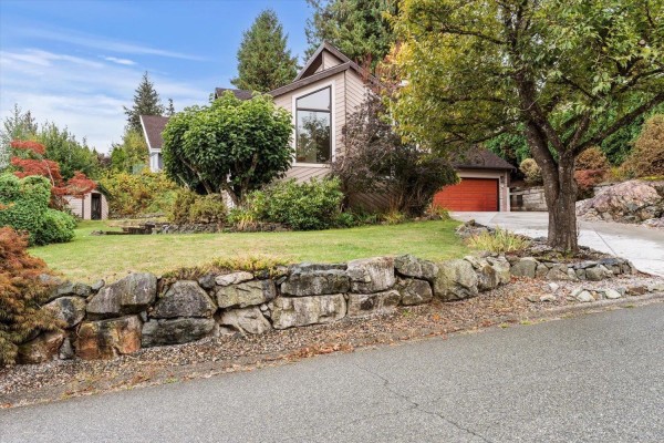 View of a beige house with stone landscaping in the foreground and a sloped lawn behind. - 47390 Swallow Crescent, Little Mountain, Chilliwack