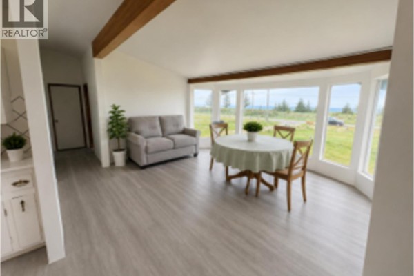 A long wooden shed with a roll-up door and a blooming tree in a grassy yard. - 474 Copper Bay Road, Skidegate/sandspit