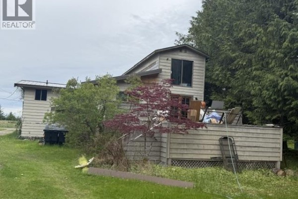 A two-story house with a large deck and surrounding greenery under an overcast sky. - 474 Copper Bay Road, Skidegate/sandspit