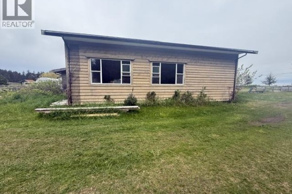 A light-colored house with a large bay window and a detached wooden garage on a gravel driveway. - 474 Copper Bay Road, Skidegate/sandspit