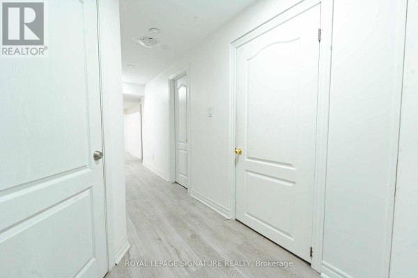 Interior hallway with light wood laminate flooring, white walls, and several white doors. - 4742 Creditview Road, Mississauga