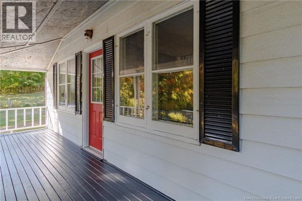 Close-up of a covered front porch with a red door, white siding, and black shutters on windows. - 4746 Route 102, Queenstown