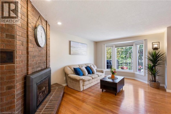 Living room with a brick fireplace, sofa, coffee table, and bay window overlooking greenery. - 475 Beechwood Drive Unit# 4, Waterloo