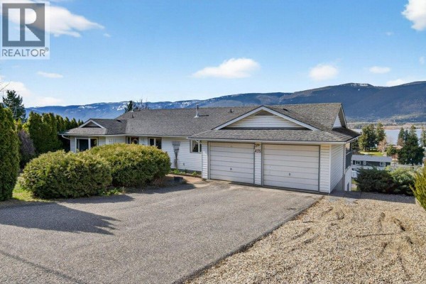 View of a white house with a double garage and paved driveway, surrounded by trees. - 4751 Lakeshore Road Ne, Salmon Arm