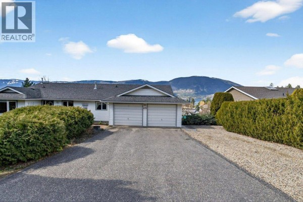 Close-up of a white vinyl-sided house with a paved walkway and manicured hedges. - 4751 Lakeshore Road Ne, Salmon Arm