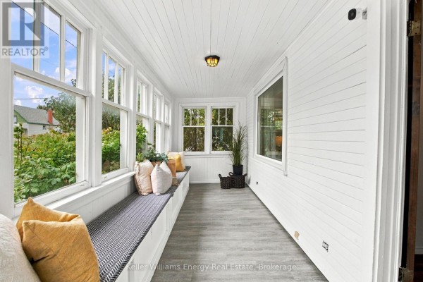 Sunroom with a long built-in bench, white wood-paneled walls, and windows overlooking greenery. - 477 Cubert Street, Oshawa