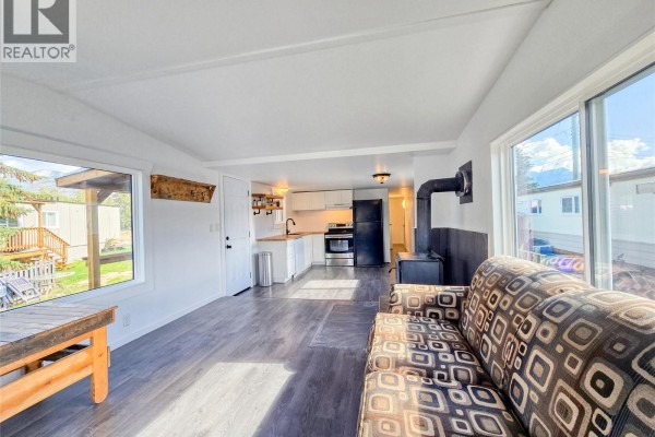 Open-concept living area and kitchen with wood stove, white cabinets, and large windows. - 4775 Wood Lane Unit# 30, Windermere