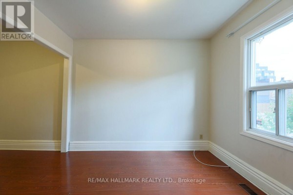 Interior view of a room with wood floors, white walls, and a large window. - 478 Logan Avenue, Toronto