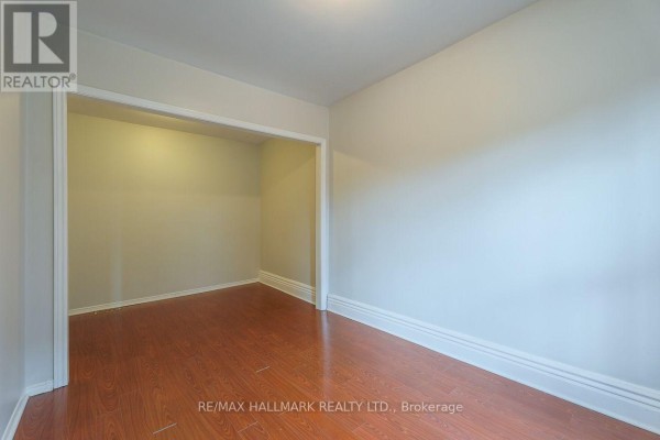 Interior view of an empty room with wood floors and an archway leading to another space. - 478 Logan Avenue, Toronto
