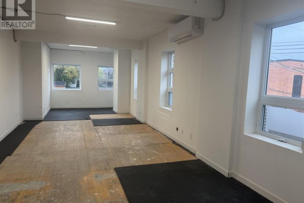 Interior view of an empty commercial space with white walls, wood floors, and windows showing exterior buildings. - 478 Queen St, Sault Ste  Marie