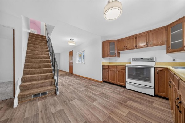 Open-concept living space with a brown carpeted staircase, wood cabinets, and vinyl plank flooring. - 478 Washington Avenue, Winnipeg