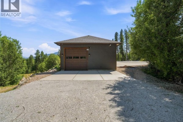 Detached single-car garage with a dark brown door and surrounding gravel driveway. - 4780 56 Street Nw, Salmon Arm