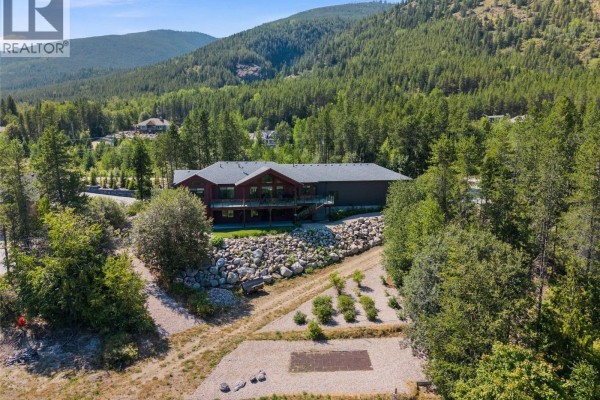Rear aerial view of the spacious home nestled amongst trees with a large rock foundation. - 4780 56 Street Nw, Salmon Arm