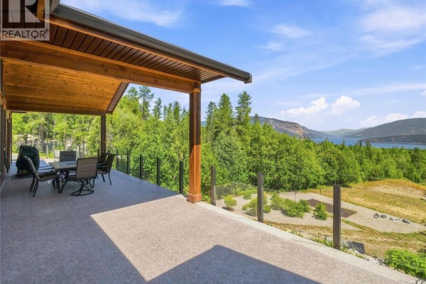 Covered outdoor patio with glass railings and furniture, offering a view of the lake and trees. - 4780 56 Street Nw, Salmon Arm