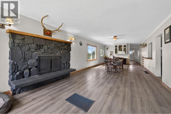 Living room with a large stone fireplace, mounted deer head, and dining area in the background. - 4780 Harrison Road, Pritchard