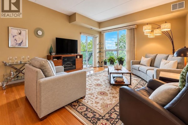 Living room with beige walls, hardwood floors, fireplace, sofa, armchair, and large window. - 4789 Riverside Unit# 504, Windsor