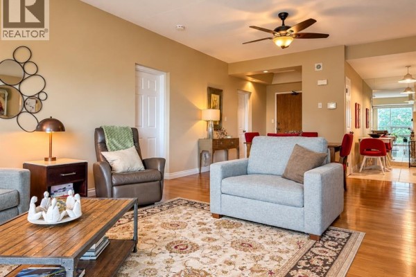 Living room with beige walls, hardwood floors, fireplace, sofa, armchair, and view of dining area. - 4789 Riverside Unit# 504, Windsor