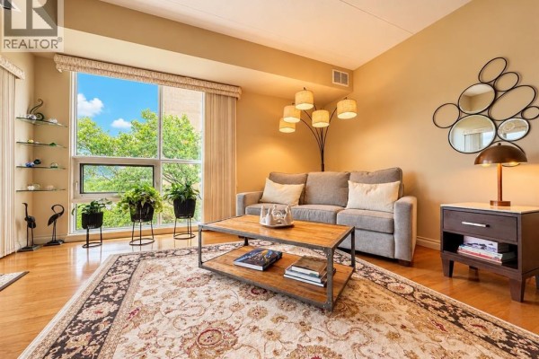Living room with beige walls, hardwood floors, sofa, coffee table, and large window with greenery outside. - 4789 Riverside Unit# 504, Windsor